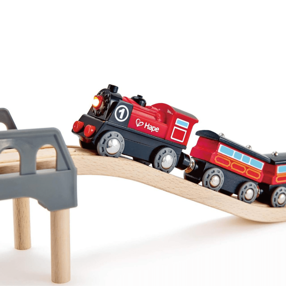 Red and black battery-powered toy train on wooden track with lighted signal