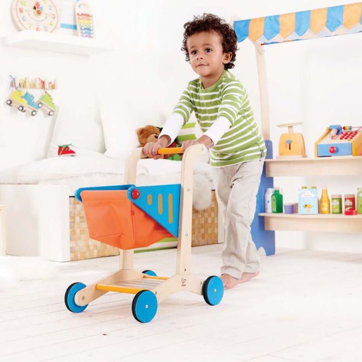 Wooden shopping cart toy with orange basket, blue side panel, and blue wheel guards.