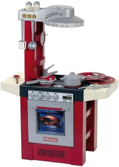 Miele toy kitchen set with red cabinet, oven door, stove burners, and cookware
