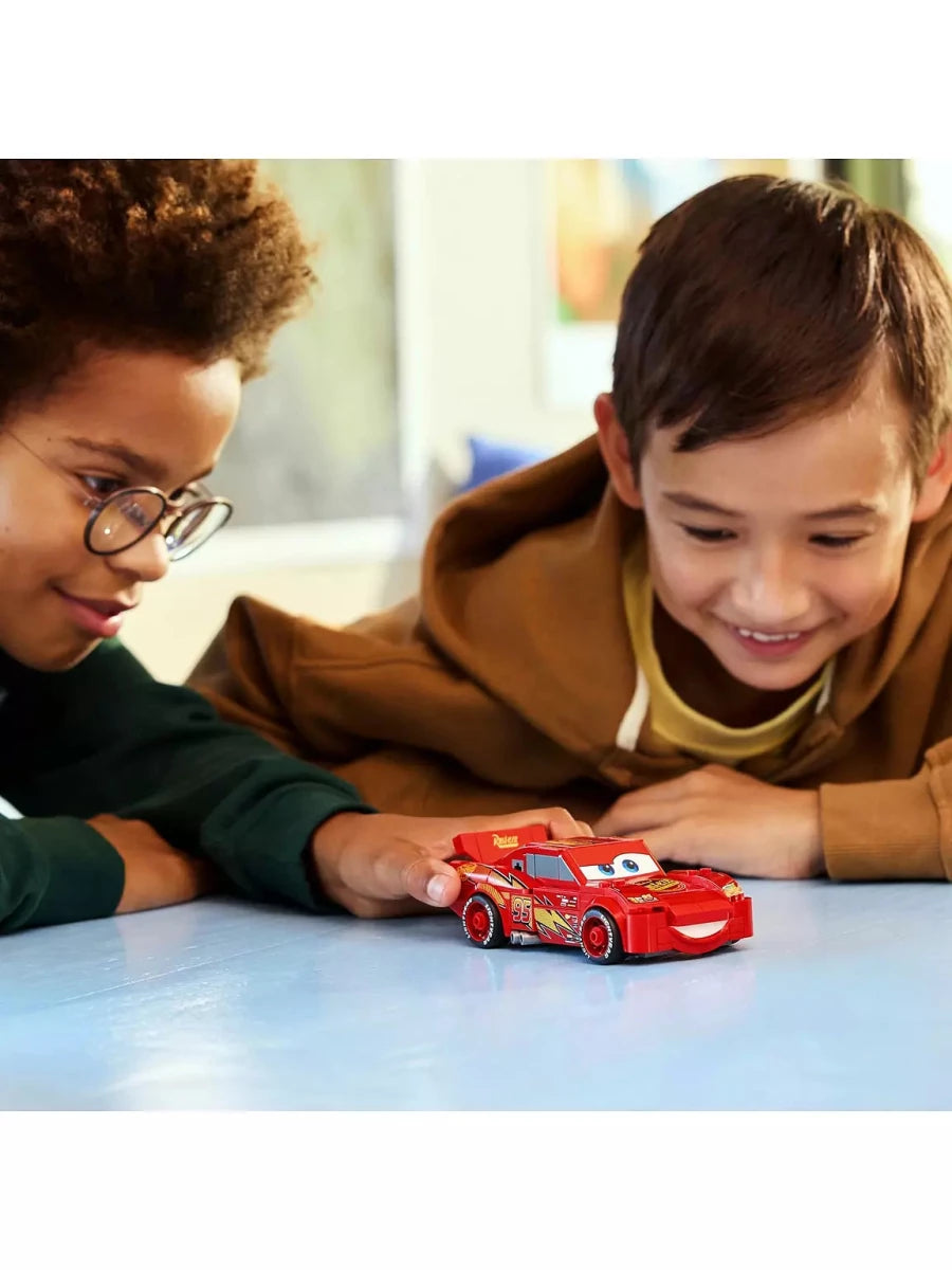 Buildable red Lightning McQueen toy car on a table, held by children