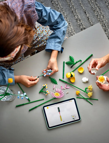 Hands assembling flower bouquet pieces: yellow petals, green stems, blue connectors