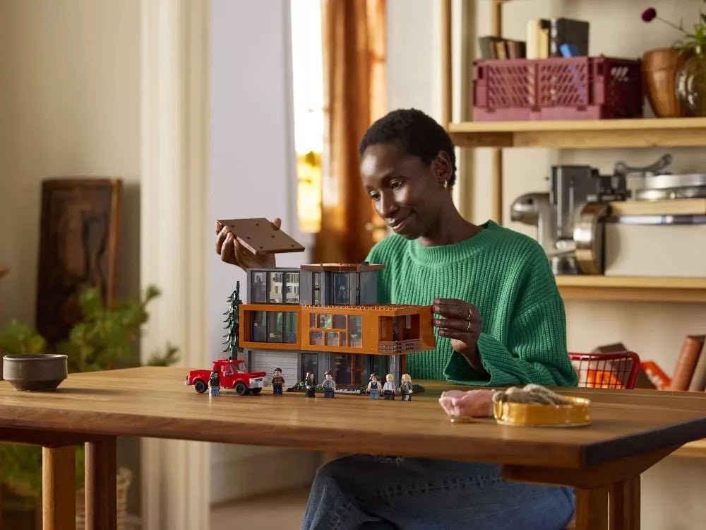 Girl holding The Cullen House LEGO set; orange two-story house model with minifigures and truck