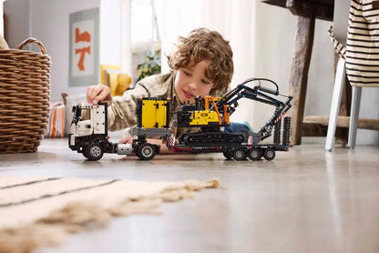 Kind spielt mit Volvo FMX Bagger-LKW LEGO Modell, gelber Aufbau und Kettenantrieb