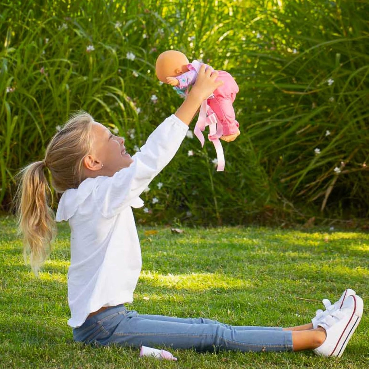 Baby doll in pink unicorn romper with blue pacifier, lifted by a child outdoors