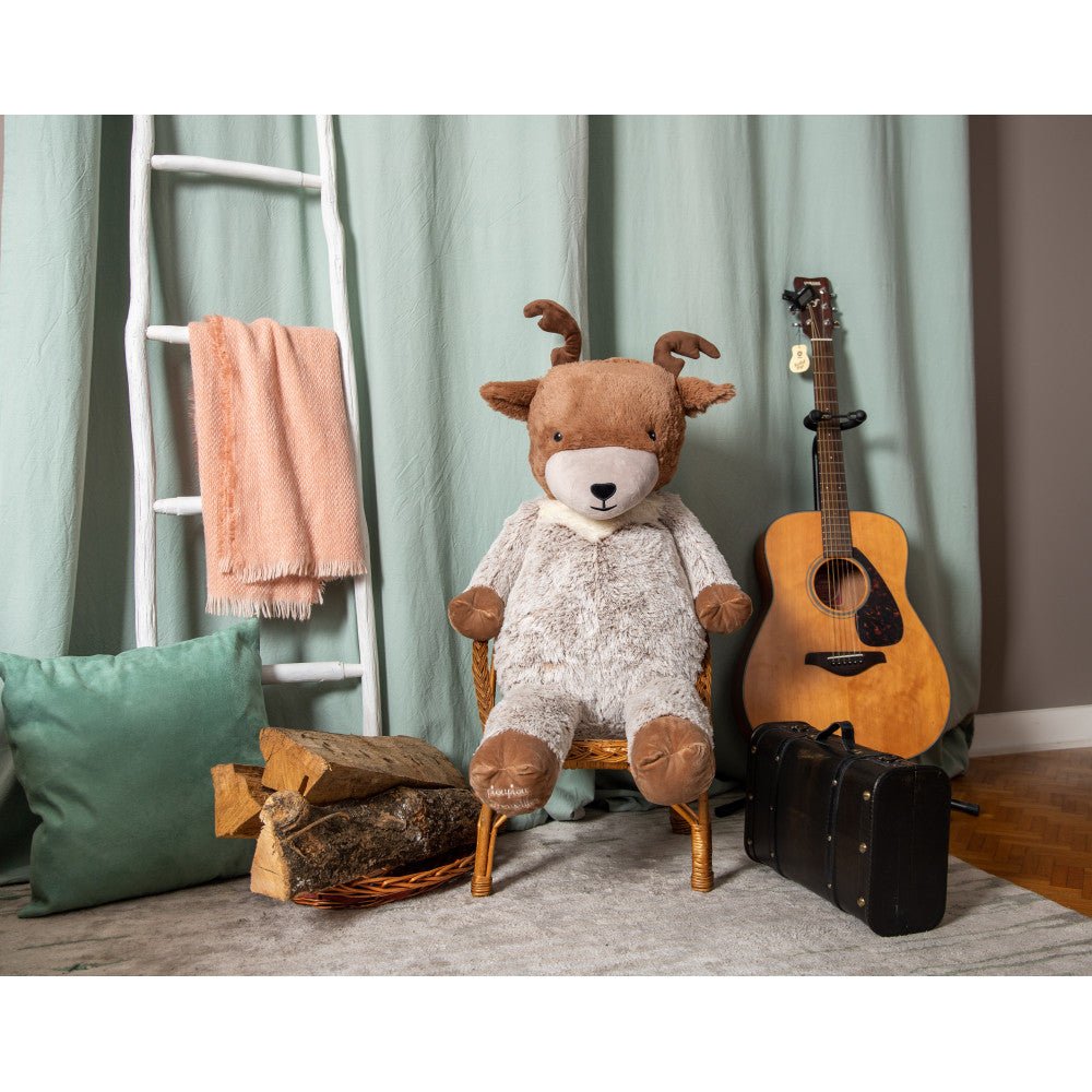 Plush reindeer toy sitting on a chair, brown antlers, white muzzle, and light gray fur.