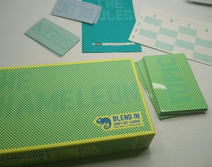 Green checkered The Chameleon board game box with stacked cards and rule sheets
