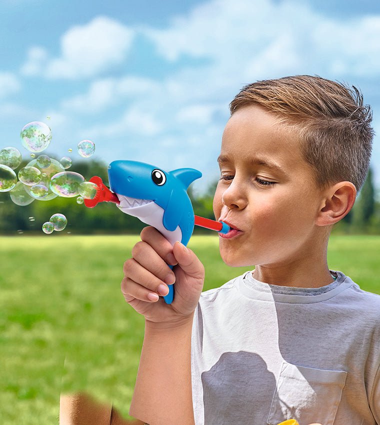 Child blowing bubbles with a blue shark bubble toy, red nozzle, and green cup